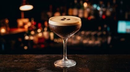 Dark espresso martini with creamy foam and three coffee beans