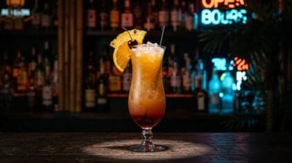 Bahama Mama cocktail in a hurricane glass with rum, coconut rum, orange and pineapple juice and a grenadine sunset