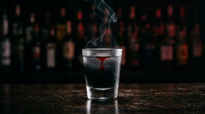 Black sambuca and mezcal shot with a single drop of bleeding red grenadine