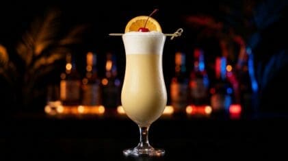 Fluffy Duck cocktail in a tall glass with creamy pastel yellow colour, frothy soda head, orange wheel and cherry garnish