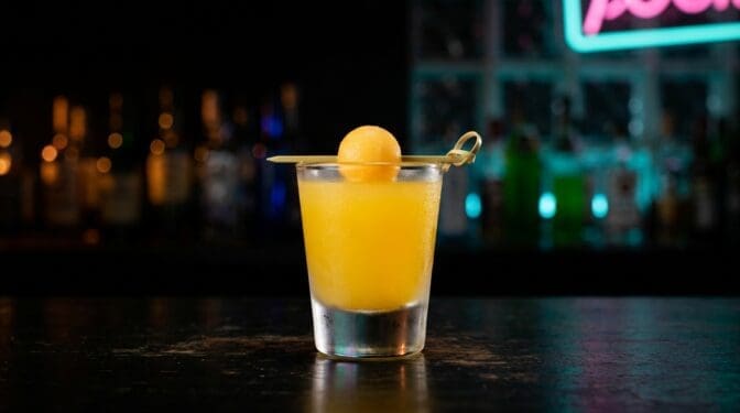 Melon Ball shot in a shot glass with bright orange-green colour from Midori, vodka and orange juice