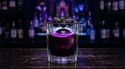 Dark blackberry rum cocktail in a heavy old fashioned glass with electric purple swirl