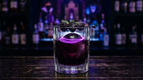 Dark blackberry rum cocktail in a heavy old fashioned glass with electric purple swirl