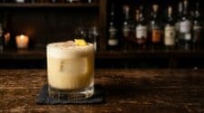 Soapy Tits cocktail in a rocks glass with a creamy foam cap on a dark bar