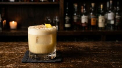 Soapy Tits cocktail in a rocks glass with a creamy foam cap on a dark bar