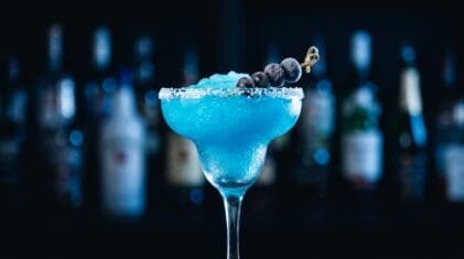 Frozen blue tequila margarita with crushed ice and a frozen blueberry skewer