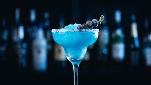Frozen blue tequila margarita with crushed ice and a frozen blueberry skewer