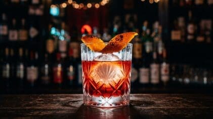 Ruby-red Negroni on a large ice sphere with flamed orange peel