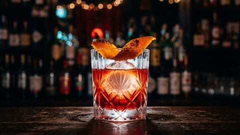 Ruby-red Negroni on a large ice sphere with flamed orange peel